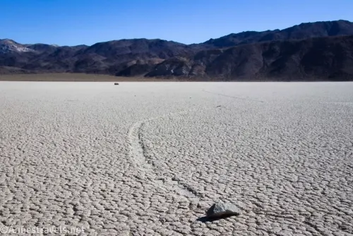 A Sailing Stone with a rock trail on the Racetrack Playa with distant mountains in the background 