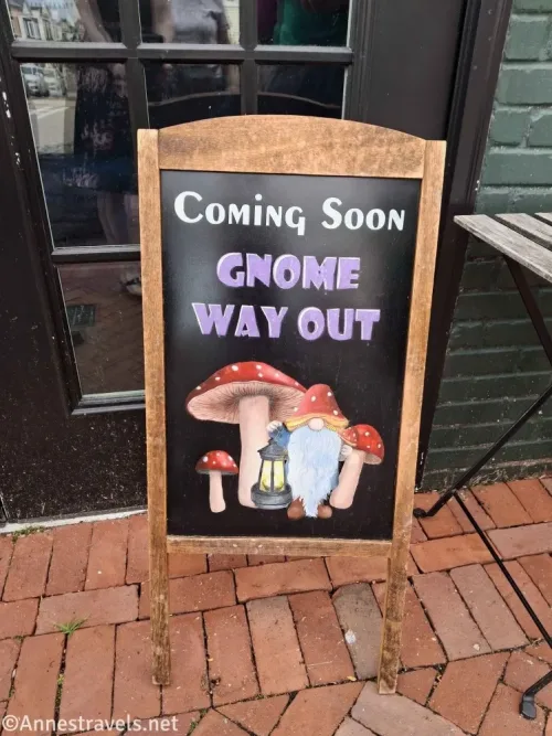 A sign with a picture of a gnome with a lantern and mushrooms and the words Coming soon Gnome Way Out
