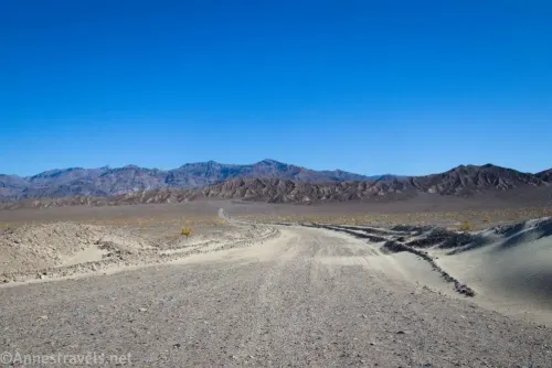 The gravel Historic Stovepipe Well Road winds across the desert toward the Kit Fox Hills and the Grapevine Mountains in Death Valley National Park, California