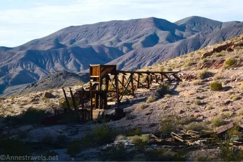 A wooden structure on a desert hillside with mountains in the background 