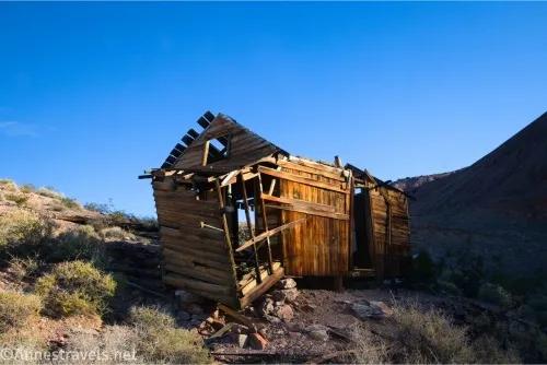 A falling-apart wooden cabin on a desert hillside against blue sky 