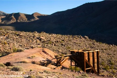 A wooden ore bin beside a slag pile in front of desert mountains