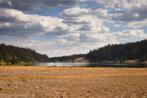 Clouds sail over forested hills, a lake, and yellow grass and rocks