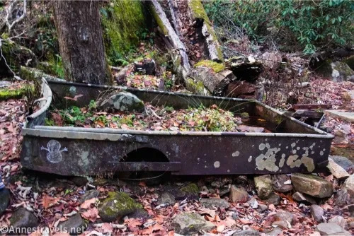 A metal wagon without its wheel filled with grass and rocks