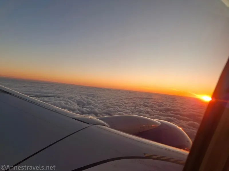 View out an airplane window of the wing, clouds, and a sunset