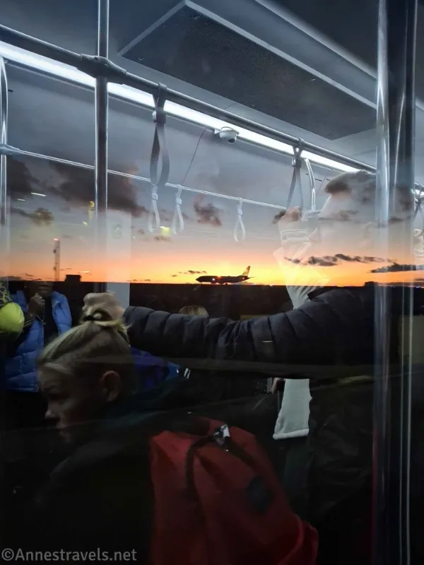 Reflections of people in a window and a silhouetted airplane against the sunset