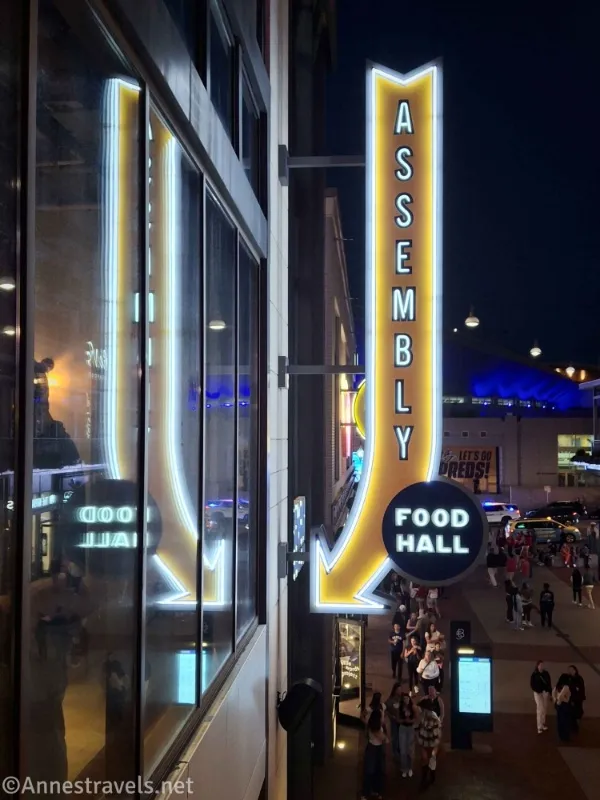 A sign that is an arrow pointing to the Assembly Food Hall with its reflection in the window 