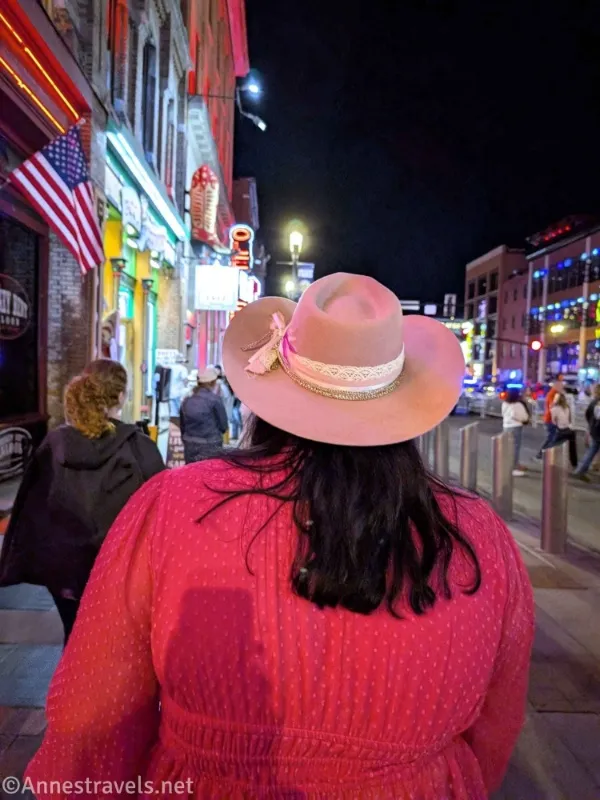 A pink cowboy hat, black hair, and a hot pink shirt of a woman on a city street with an American flag 