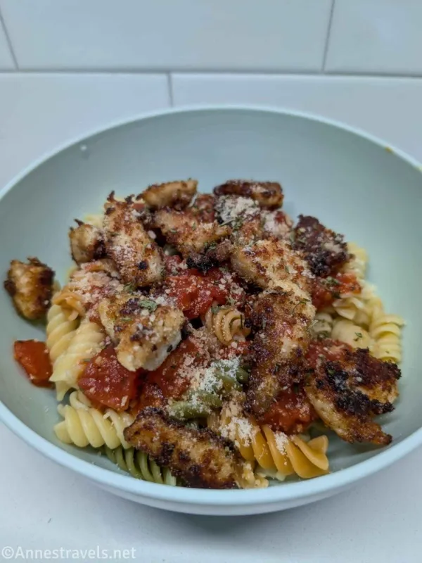 A pasta dish topped with tomatoes and fried chicken in a blue bowl 