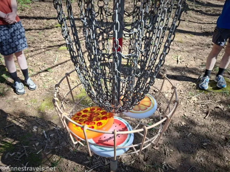 Three colorful, food-themed frisbees in a metal disc golf cage with two people standing nearby 