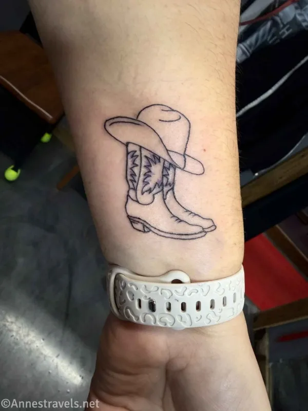 Cowboy boots and a cowboy hat on the arm of a woman with a white watchband
