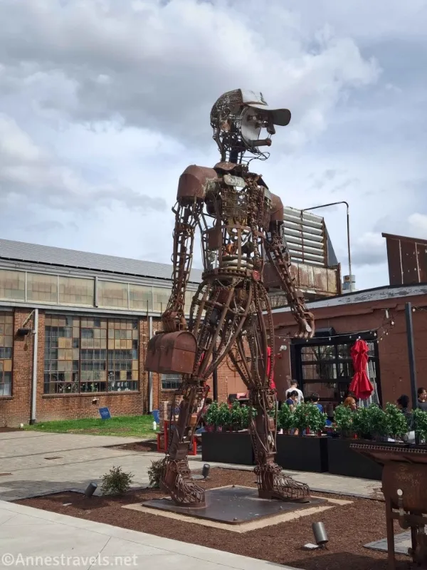 A statue made of scrap metal in front of an old factory and red umbrellas 
