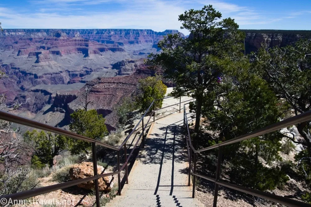 Concrete stairway bordered by metal pole fencing in front of the Grand Canyon