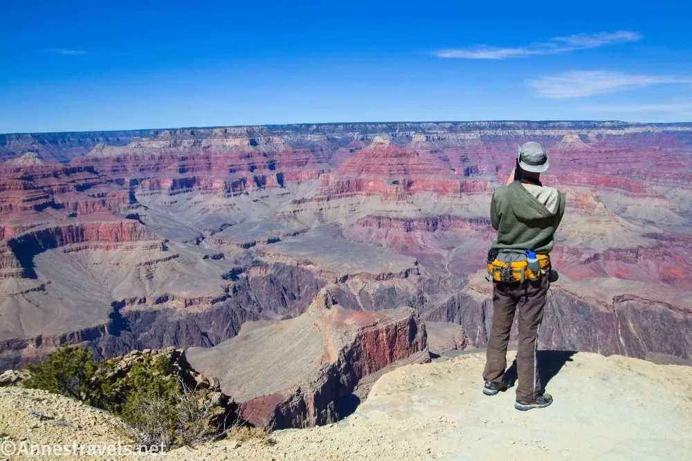 A hiker with a yellow pack stands on the edge of the Grand Canyon