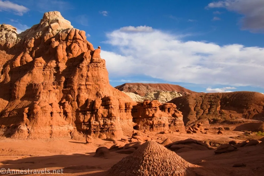 Red badland rock formations beside clouds in a blue sky
