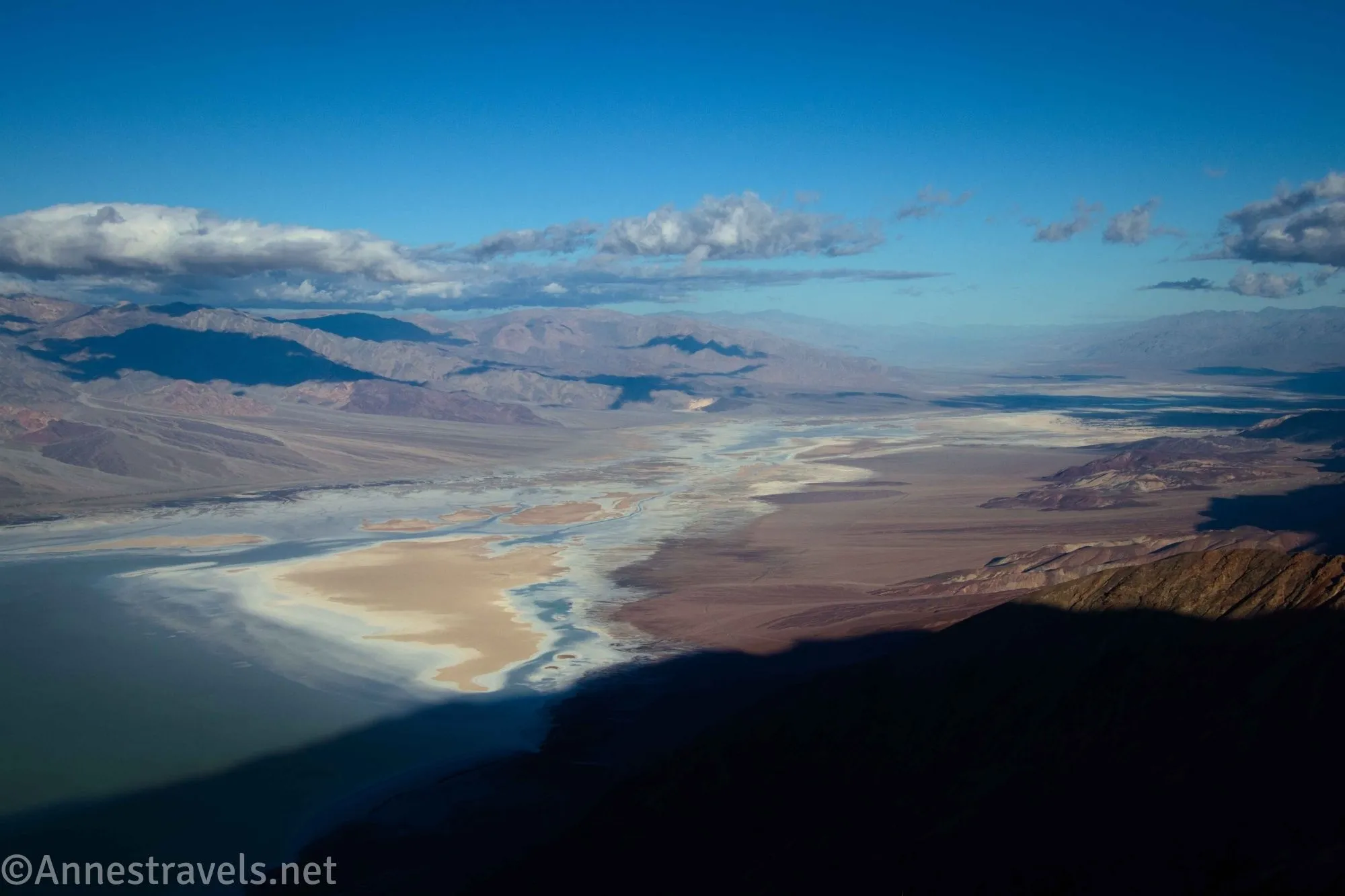 Views into a desert valley with a lake with clouds above and blue skies