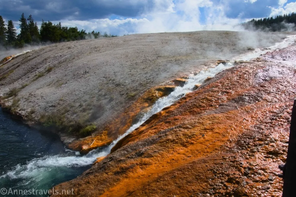 A waterfall flowing over orange ground with gray ground behind at the Midway Geyser Basin in Yellowstone National Park