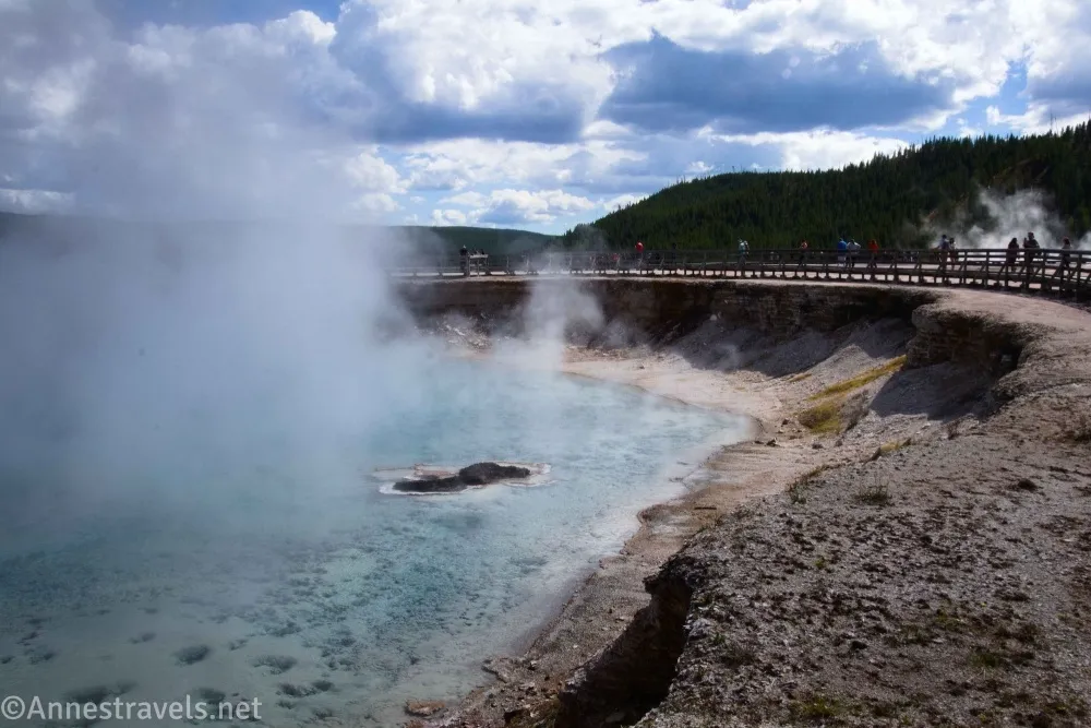 Boardwalk beside the steaming blow water of Excelsior Geyser and below clouds in Yellowstone National Park
