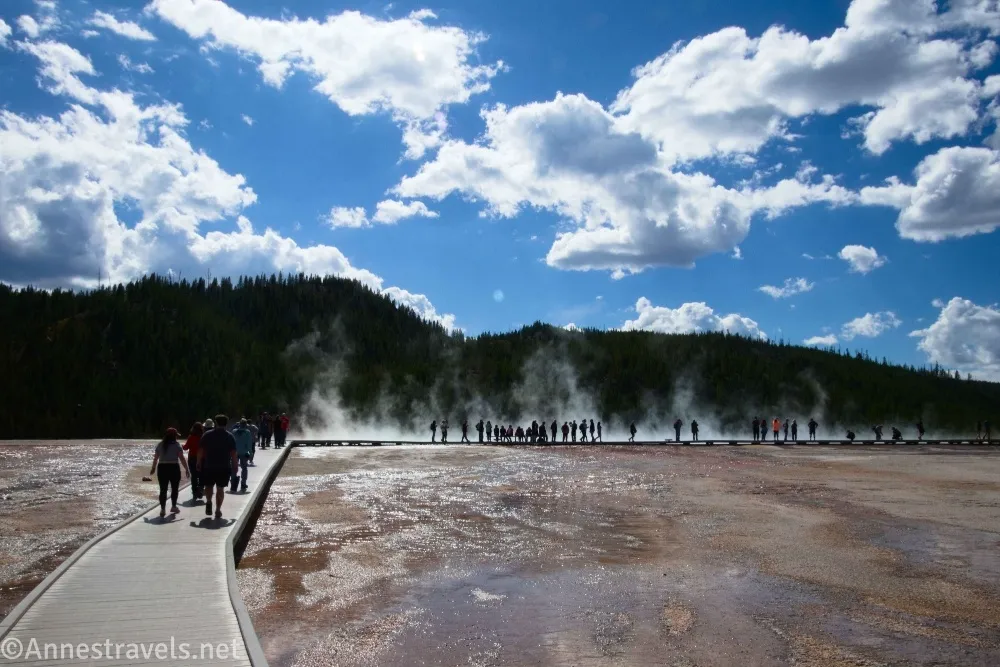 Clouds over dark hills and a boardwalk with many people near the Grand Prismatic Spring in the Midway Geyser Basin of Yellowstone National Park