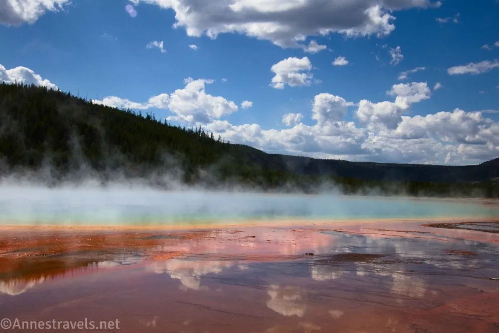 Clouds sail over dark hills and the colorful reflections in the Grand Prismatic Spring, Yellowstone National Park