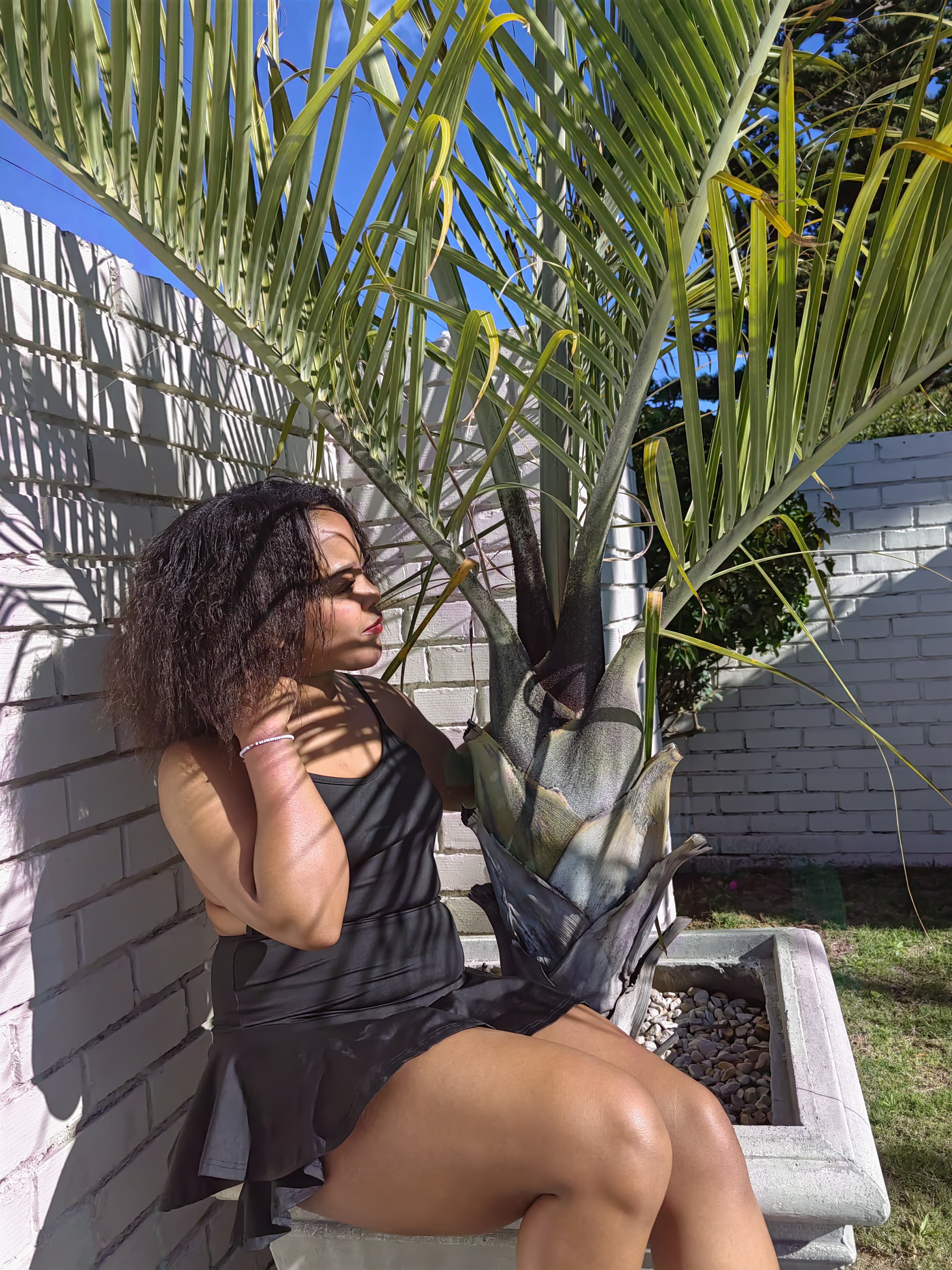 Black ruffle dress by a white brick wall