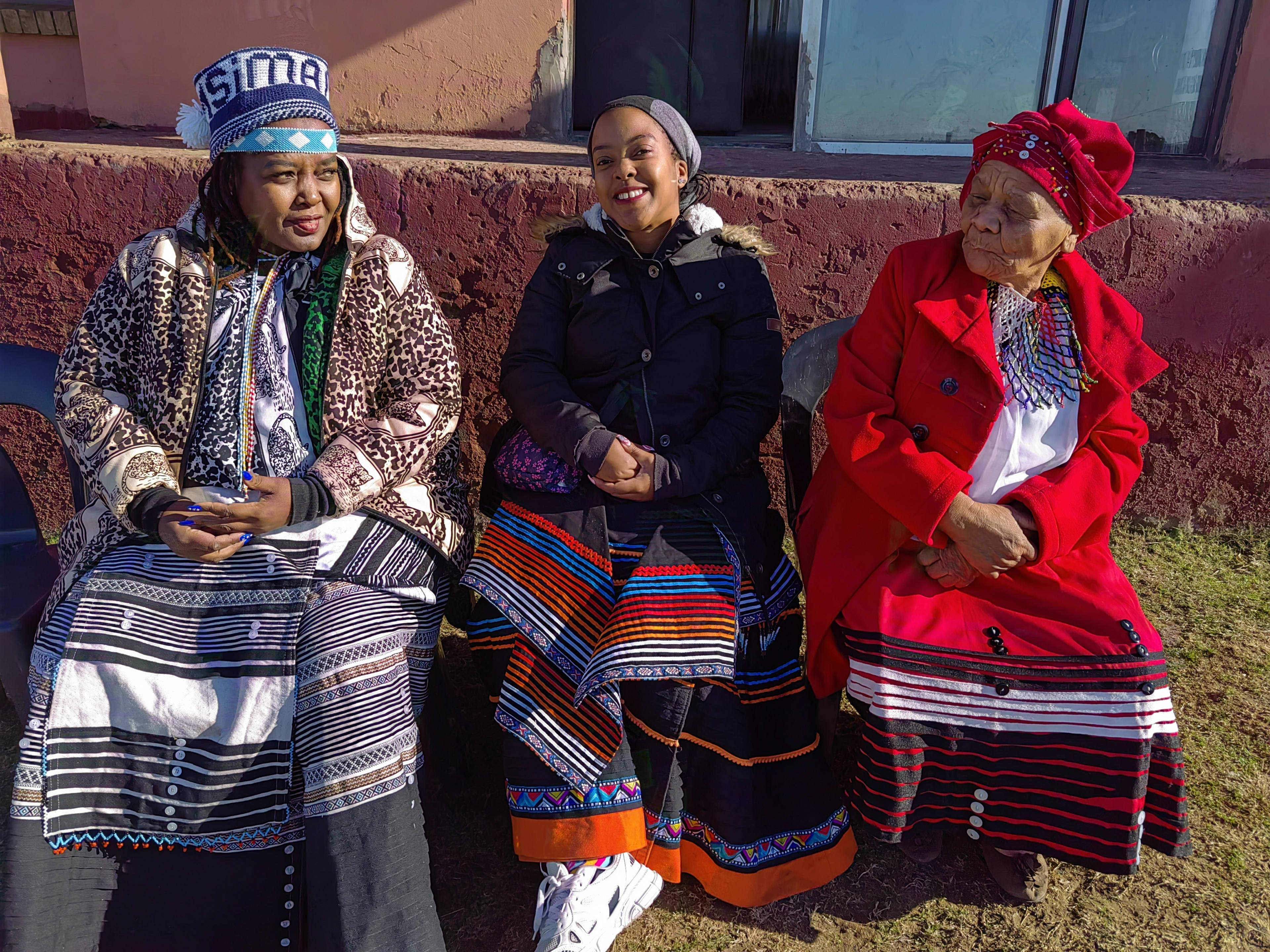Between two elders in Xhosa dress, winter light and laughter