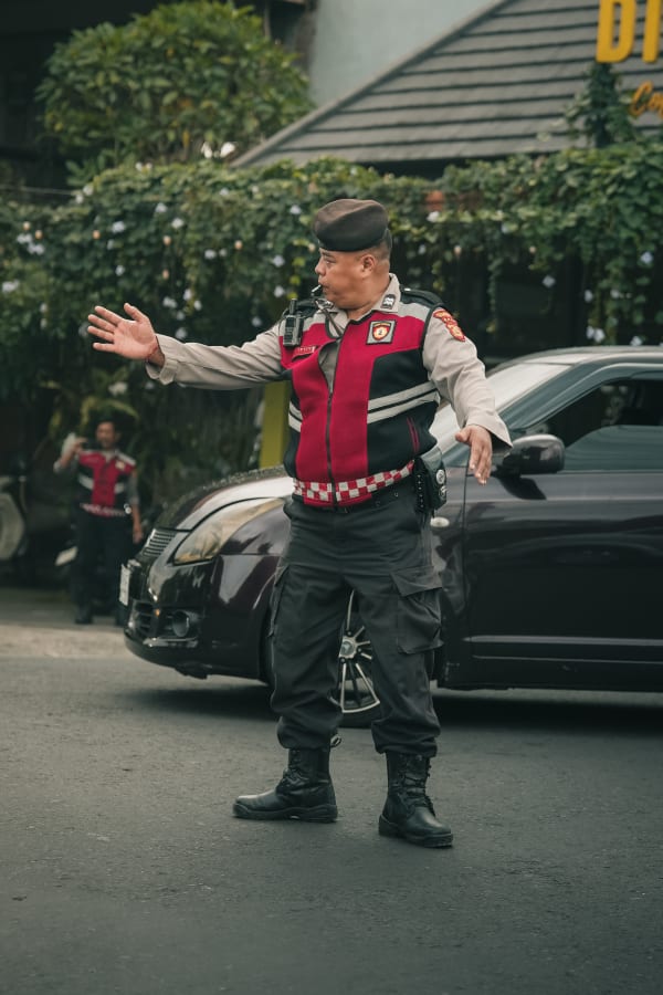 Balinese KORPS SABHARA traffic police officer in uniform directing street activity, Bali, Indonesia, with lush foliage.