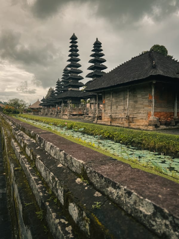 Pura Taman Ayun temple in Mengwi, Bali under an overcast sky, with multi-tiered meru towers, traditional structures, and a serene lotus pond.