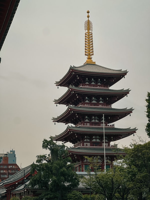 Senso-ji Pagoda, Taito, Japan. Five-story Buddhist temple, dark red tiers, grey tiled roofs, golden finial under overcast sky.