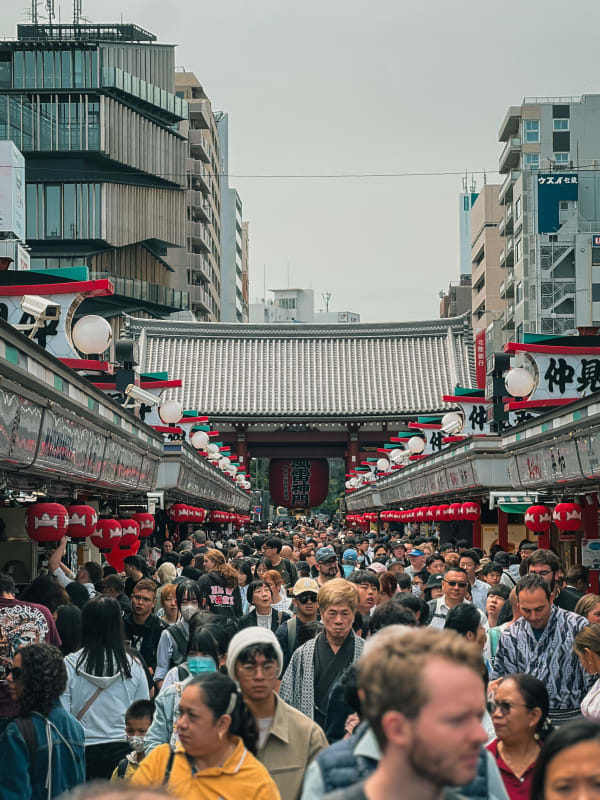 Crowded Nakamise-dori market street leading to Senso-ji Temple Hozomon Gate, Tokyo, Japan. Red lanterns, shoppers, traditional stalls.