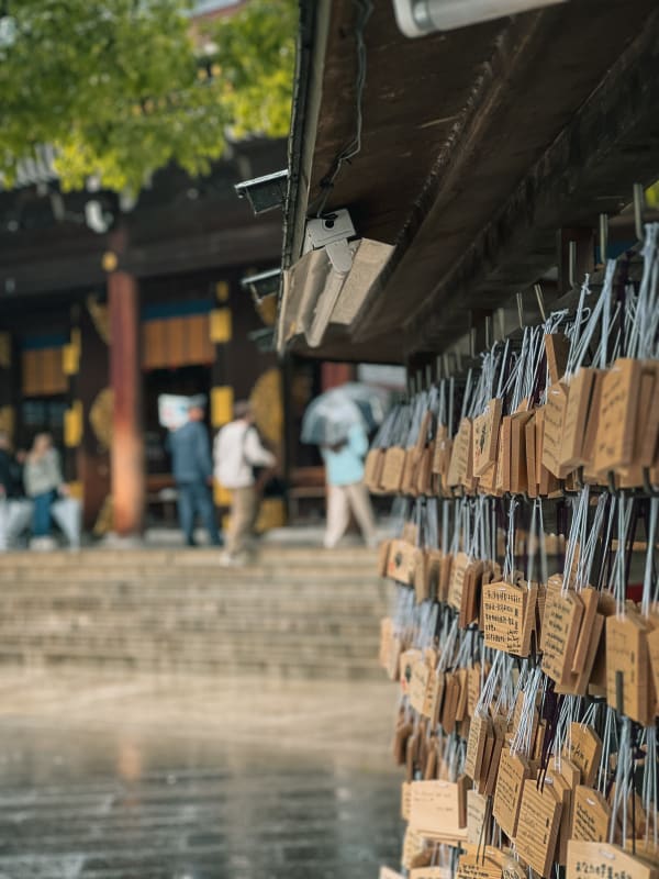 Close-up of numerous wooden Japanese ema votive tablets hanging at a shrine in Shibuya, Tokyo, on a soft, rainy day.