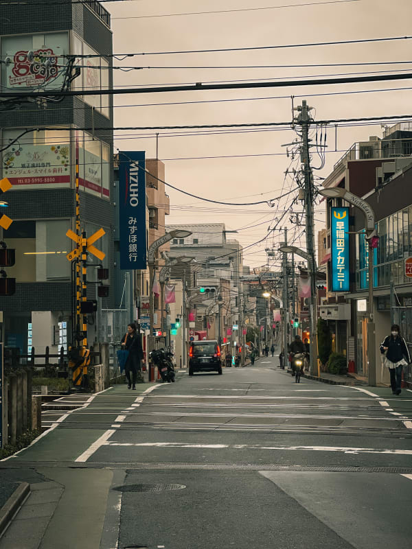 Urban street scene in Nerima, Tokyo, Japan with dense power lines, a train crossing sign, pedestrians, shops, and a Mizuho bank sign.