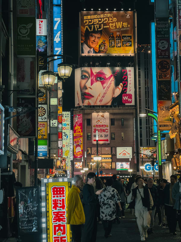 Vibrant night street view in Kabukicho, Shinjuku, Japan. Neon signs, large billboards, people walking below.