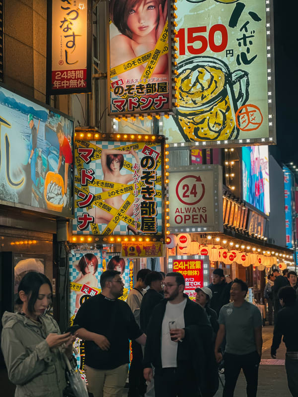Busy night street in Shinjuku, Tokyo, Japan with bright Japanese neon signs, anime ads, Kizuna Sushi, and pedestrians.
