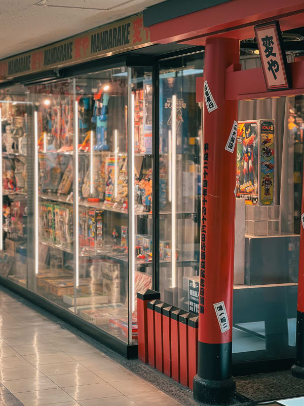 Mandarake collectible shop in Nakano, Japan, featuring display cases with anime figures, manga, and vintage toys. Red torii entrance.