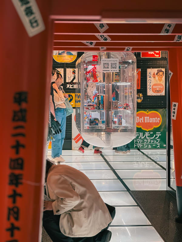 Nakano, Japan: Vintage Japanese advertising posters behind a clear collectible toy display, framed by blurred red architectural pillars.