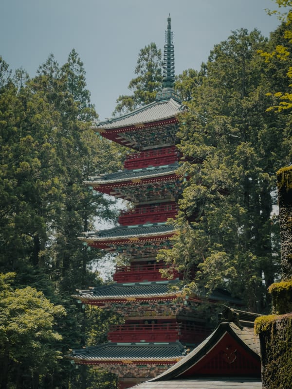Five-story pagoda at Toshogu Shrine, Nikko, Japan, vibrant red with intricate carvings, surrounded by lush green forest under clear sky.