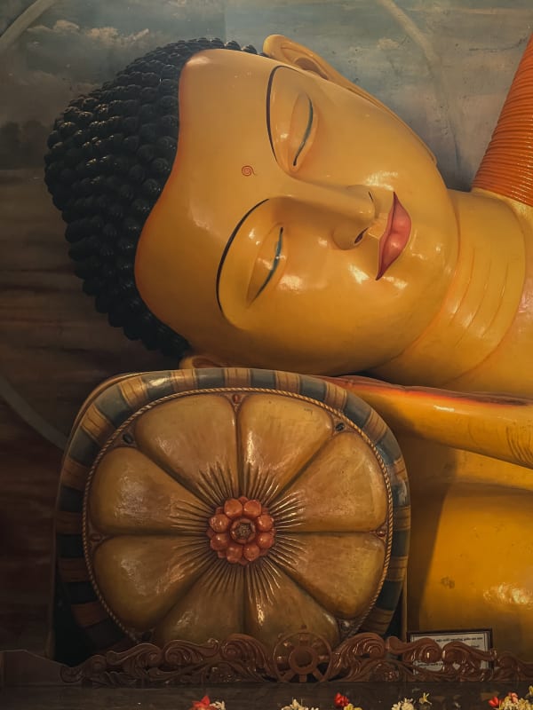 Close-up of a golden reclining Buddha statue, serene expression, black hair, blue-painted background, Buddhist temple in Maharagama, Sri Lanka.