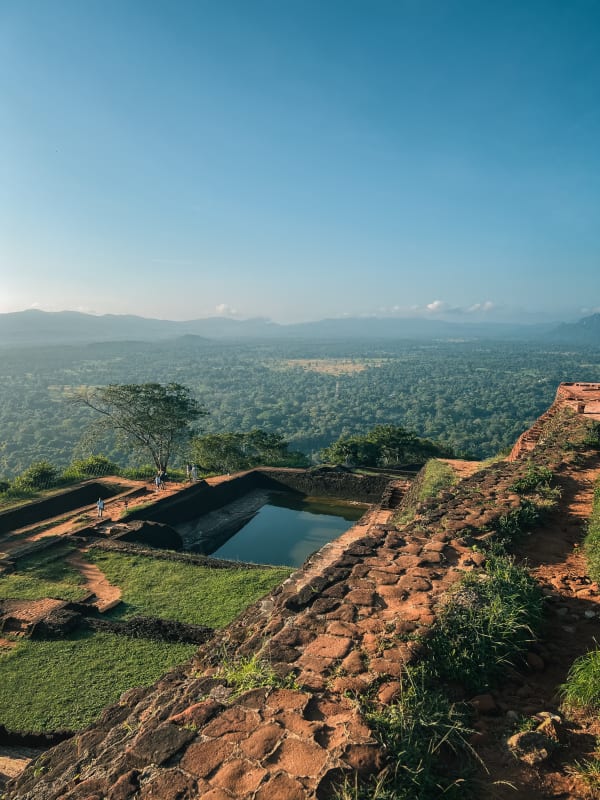 Sigiriya, Sri Lanka: Ancient palace ruins, terraced water gardens, lush jungle, distant mountains under a blue sky.