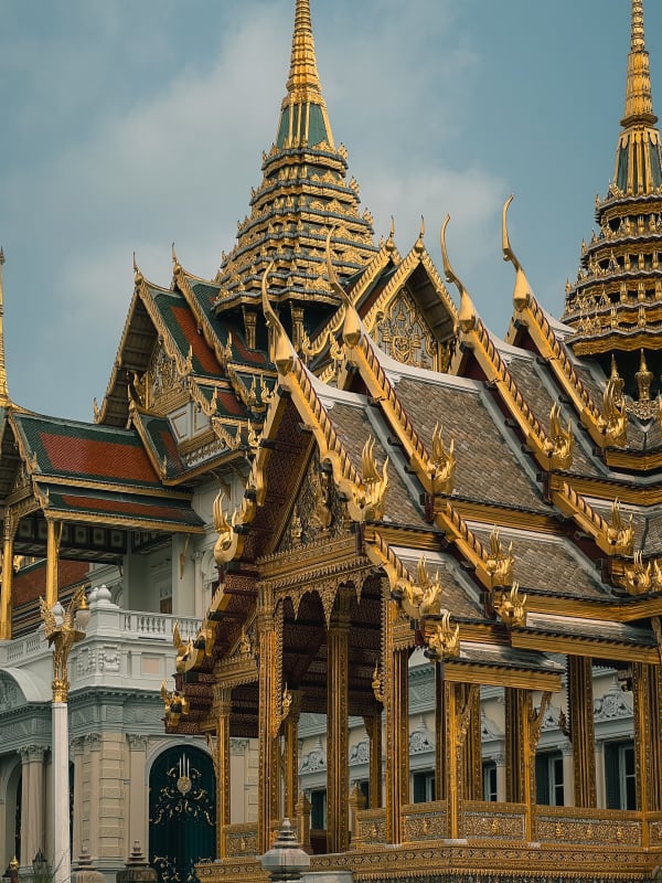 Gilded spires, multi-tiered roofs, and intricate gold ornamentation of a traditional Thai temple or palace in Bangkok, Thailand.