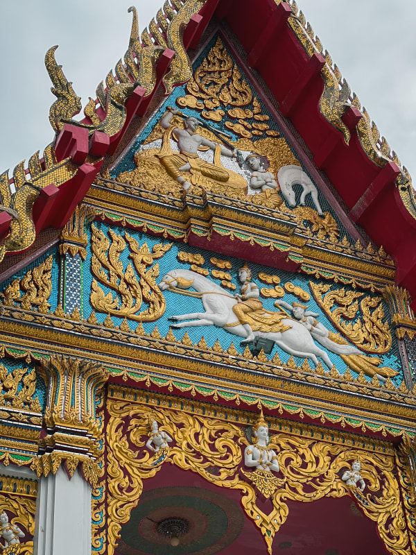 Ornate Thai temple gable, Bang Pakong, Thailand. Gilded gold leaf reliefs, red eaves, blue mosaic, mythical figures, warrior on horse.