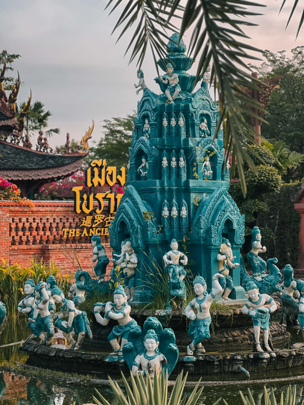 The Ancient City, Thailand: Intricate teal and white statues surrounding a multi-tiered fountain, lush greenery, ornate Thai architecture.