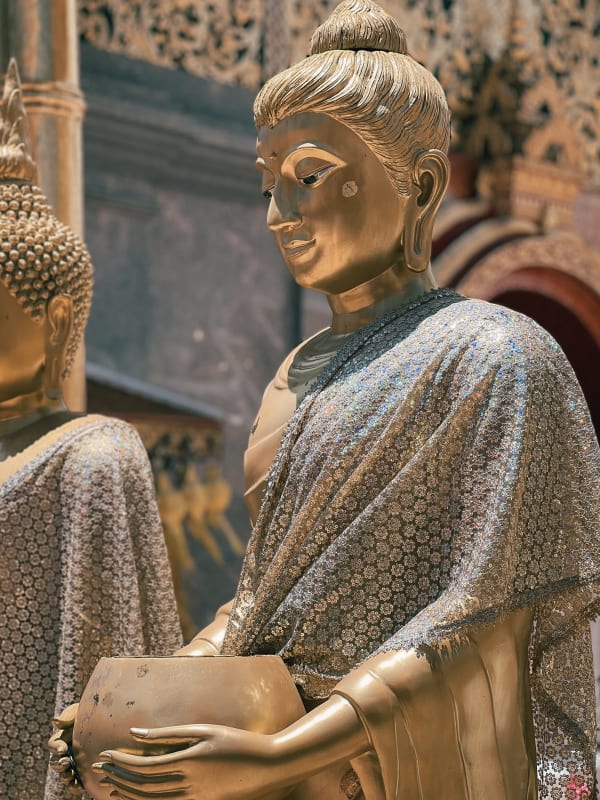 Golden Buddha statue holding alms bowl in Mueang Chiang Mai, Thailand. Shimmering floral patterned robe, intricate details, spiritual.