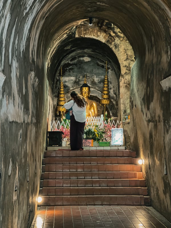 Worshipper before golden Buddha statue in ancient arched tunnel, Wat Umong, Chiang Mai, Thailand, low light.