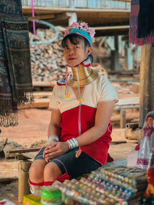 Kayan 'Long Neck' woman in traditional golden neck rings, red top, flower headband, at market in Chiang Rai, Thailand.