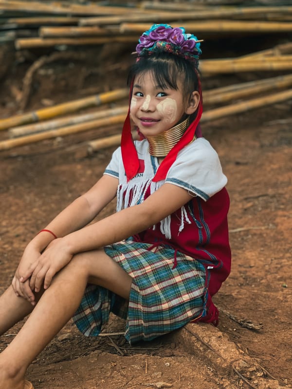 Young Kayan Long-Neck girl smiling, wearing brass neck rings, floral headpiece, traditional dress in Chiang Rai, Thailand.