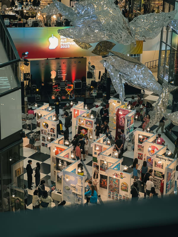 Overhead view of Mango Art Festival 2025 at River City Bangkok, art stalls, crowds, whale sculptures, checkered floor.