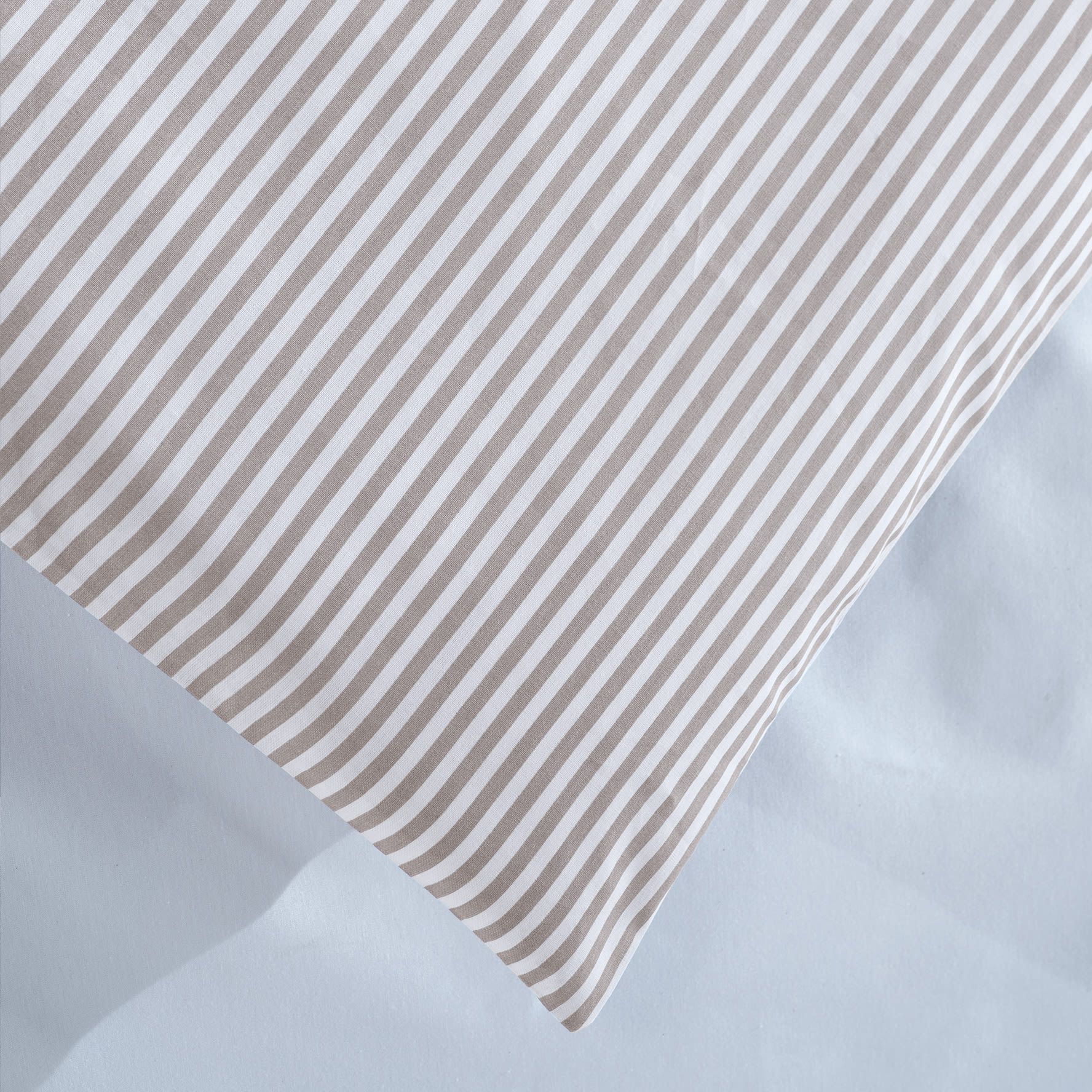 Pudebetræk med diagonale beige og hvide striber. Det ligger på lyst blåt sengetøj.