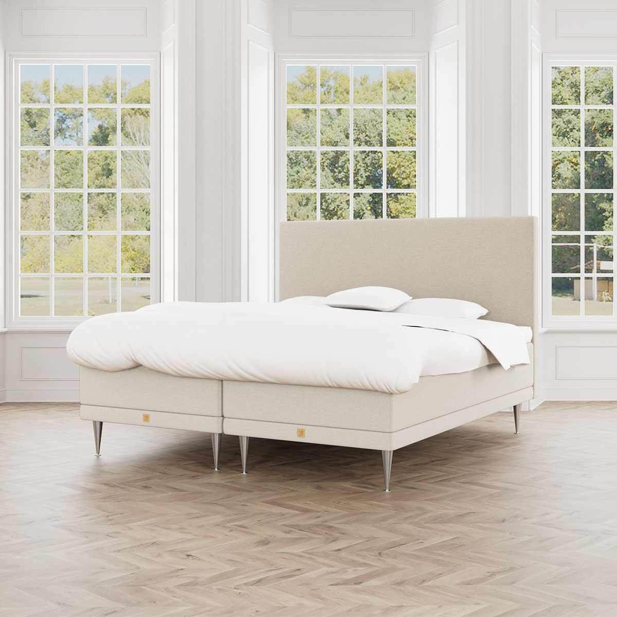 En beige boxmadras fra MasterBed Aria med sengegavl, hvidt sengetøj og cocktailben, set forfra.