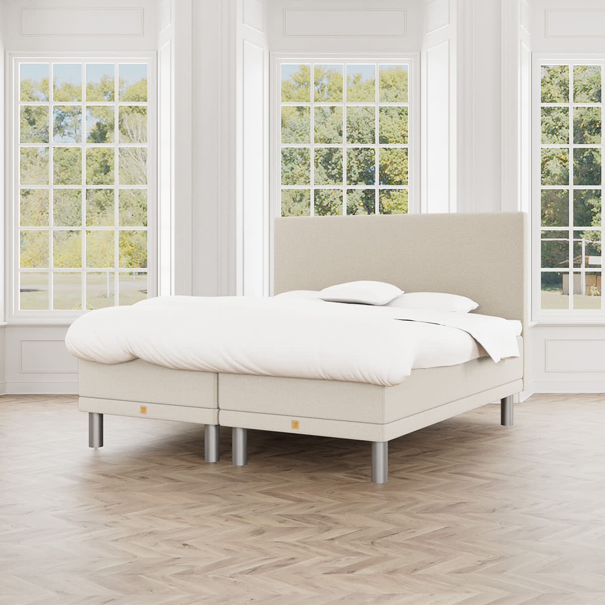 Beige boxmadras fra MasterBed med Aria sengegavl, hvidt sengetøj og runde ben, set forfra.